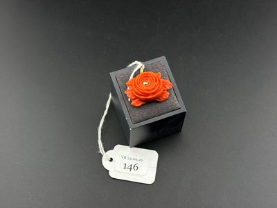 an orange flower brooch on a black box with a price tag