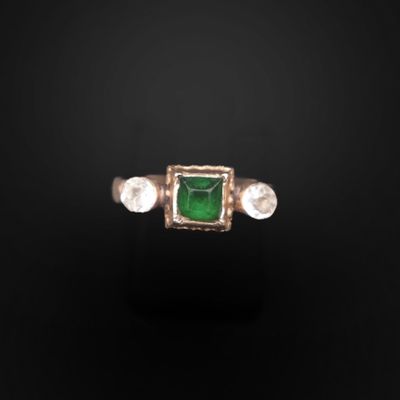 un gros plan d'une bague ornée d'une pierre verte entourée de trois pierres blanches