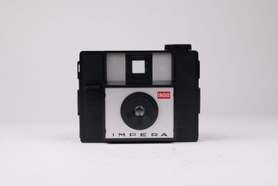 une vieille photo représentant un appareil photo posé sur une surface blanche, avec un fond blanc