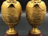 pair of gold vases on wooden bases on a black background