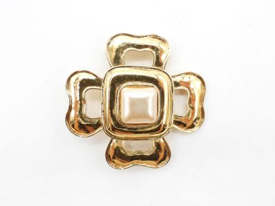 a close up of a gold cross brooch with a pearl center