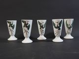 four white vases with green leaves on them sitting on a black surface