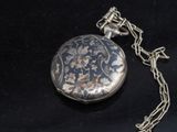 une montre de poche en argent attachée à une chaîne, posée sur une surface noire