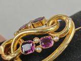 a close up of a gold brooch with purple stones on it