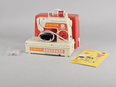 une machine à coudre rouge et blanche à côté d'un livre jaune et blanc