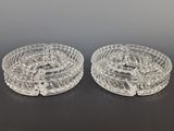 two clear glass ashtrays on a table with a black background