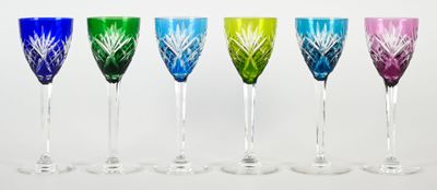 six verres à vin de couleurs différentes alignés sur une surface blanche