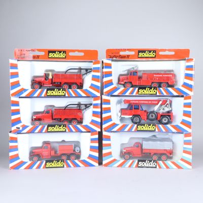 quatre camions rouges miniatures dans une boîte posée sur une surface blanche