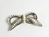 an image of a white bow brooch with pearls on it