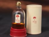 une petite bouteille en verre avec un bouchon rouge à côté d'une tasse blanche