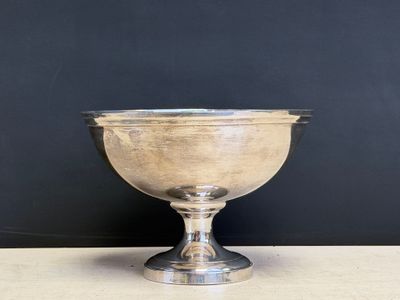 an antique silver plated bowl on a pedestal against a black wall
