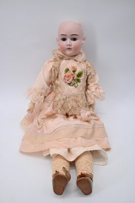 une vieille poupée vêtue d'une robe rose et de chaussures marron, assise sur une surface blanche