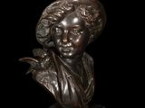 bronze bust of a young boy with a hat on a black background