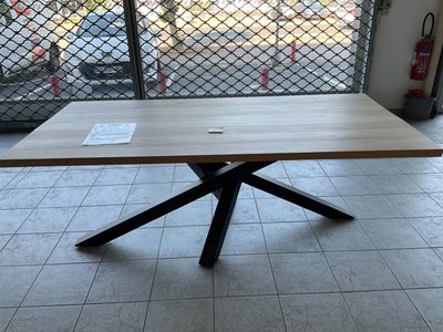 une table en bois avec un piètement en croix métallique au milieu d'une pièce
