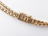 a close up of a gold bracelet with a clasp on a white surface
