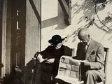 a man and a woman sitting on a bench reading a newspaper
