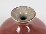 a red vase with a brown rim sitting on a white surface