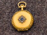 une image représentant une montre de poche en or ornée d'une pierre bleue au centre