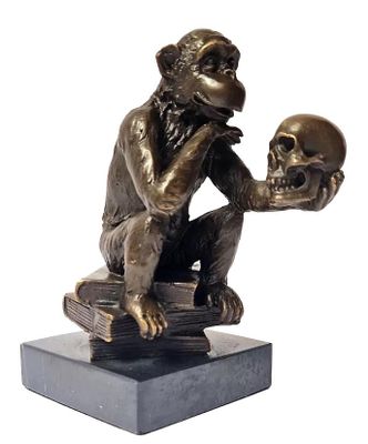 bronze statue of a monkey holding a skull on a book