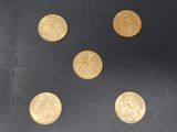 six pièces d'or sont disposées en ligne sur une surface noire