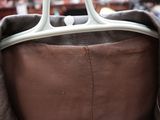 a brown leather jacket with a white handle hanging on a hanger