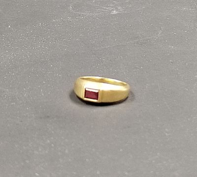 une bague en or sertie d'une pierre rouge, posée sur une table