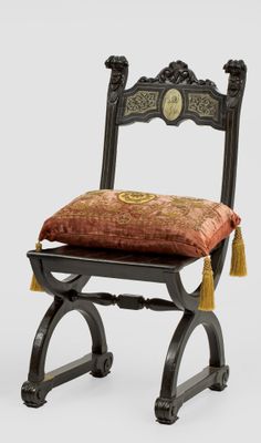 a black chair with a red cushion and a gold tassel on it