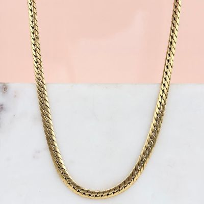 un gros plan d'un collier en or posé sur une surface en marbre
