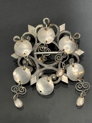 une broche ancienne en argent posée sur une surface noire avec un fond noir