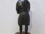 statue d'un homme debout sur un socle en bois, de dos à la caméra