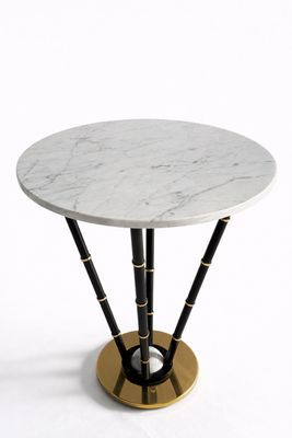 une table en marbre blanc avec des pieds en bambou noir et un socle doré
