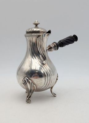 une cafetière ancienne en argent avec une poignée noire sur une surface blanche