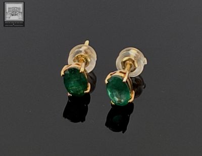 pair of emerald earrings on black surface with reflection