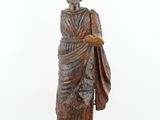 une vieille statue représentant un homme tenant un sac, posée sur un socle en bois