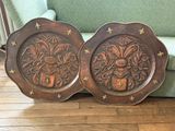 une paire d'assiettes anciennes en bois sculpté posées sur un parquet, à côté d'un canapé vert
