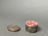 a small silver container with a red lid next to a coin