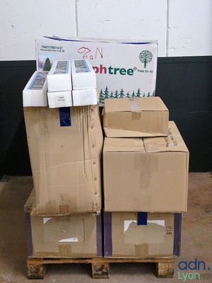 des cartons empilés sur des palettes devant un mur sur lequel est accrochée une pancarte