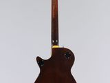 a brown guitar hanging from a string on a white wall