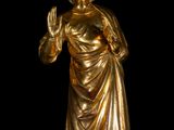 gold statue of a woman in a draped dress with her hands raised