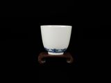 une tasse blanche posée sur un socle en bois, sur fond noir