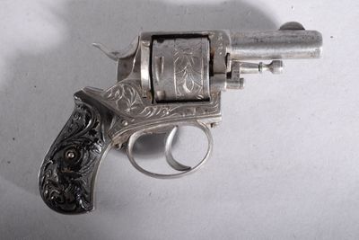 un revolver argenté posé sur une surface blanche, avec une ombre projetée sur le mur