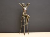 statue en bronze représentant une femme assise sur un tabouret, les mains levées