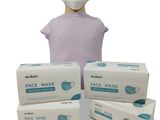 une personne portant un masque à côté de trois boîtes de masques jetables