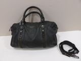 black leather handbag with zippers and a leash on a white surface