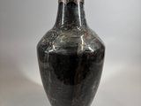 an old black vase sitting on top of a white table