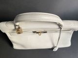 the white purse is sitting on the table with a metal handle