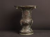 un vase antique en bronze posé sur une table, sur un fond sombre
