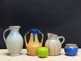 four different vases sitting on a table with a green apple