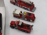 Plusieurs camions de pompiers miniatures sont rangés dans une boîte posée sur une table