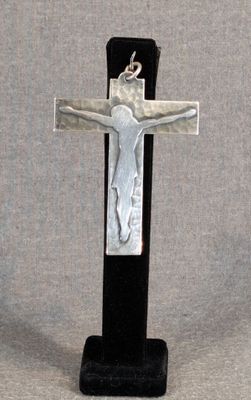 une croix argentée posée sur un socle noir, sur fond gris